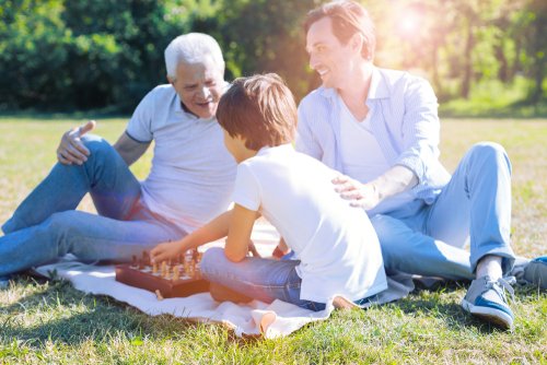 Grandfather, father, and son playing chess in the park.