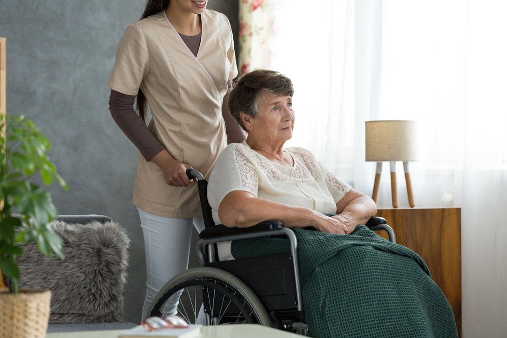 Woman caregiver pushing elderly patient in a wheel chair