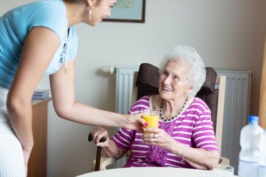Dementia Caregiver Assists Senior Woman At Meal